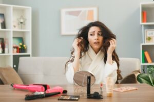 Une jeune fille, l'air mécontente, s'est agrippée aux cheveux d'une autre jeune fille assise à la table avec des produits de maquillage dans le salon. maquillage le jour d'une greffe de cheveux