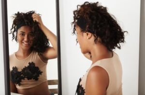 Une femme noire essaie une perruque et se regarde dans le miroir- Cheveux afro : résultats réels avant/après
